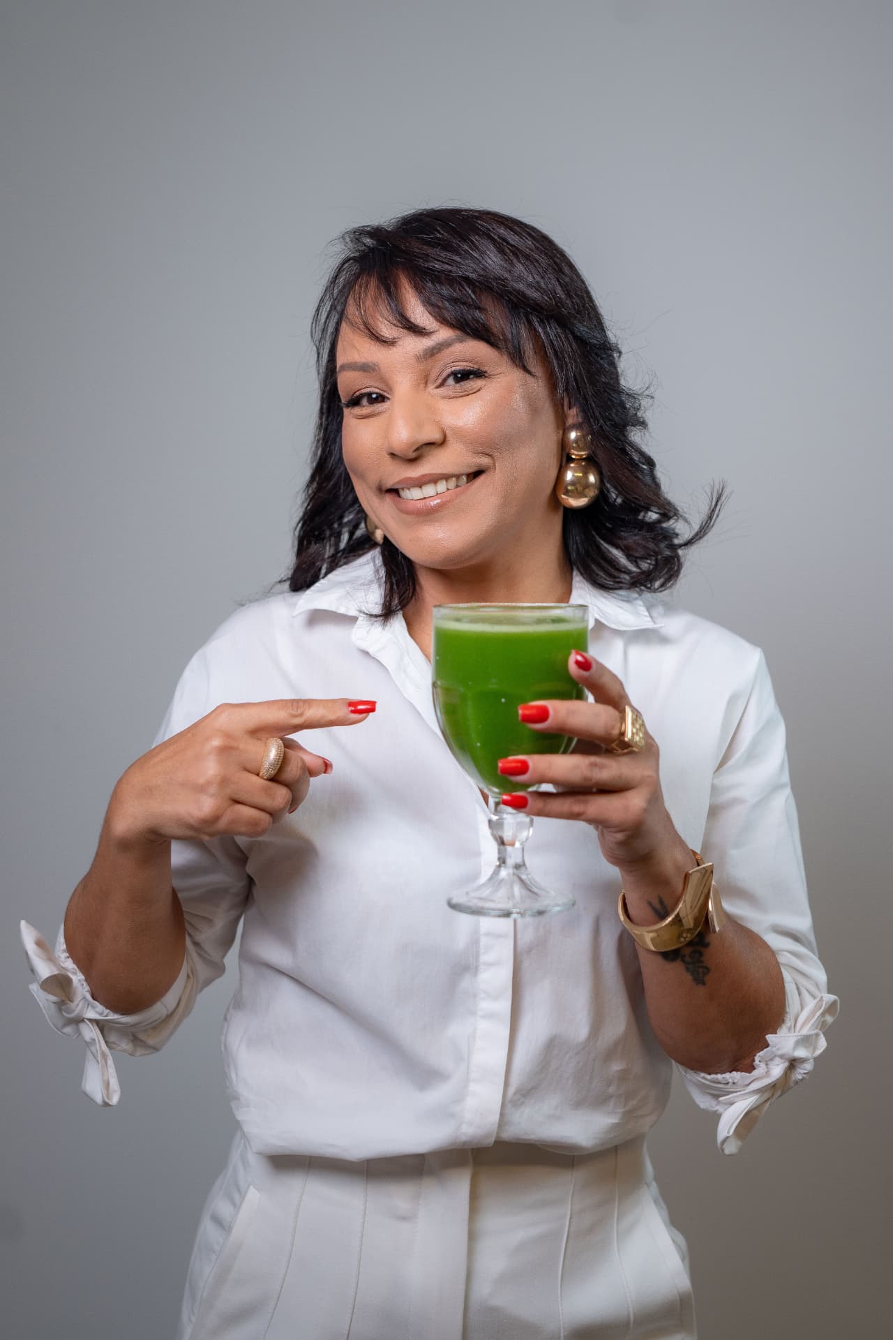 A nutricionista Catia Moraes sorrindo e segurando uma taça de suco verde